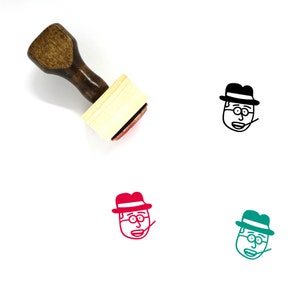 Puede incluir: Un sello de goma de madera con una almohadilla de tinta roja. El sello presenta una ilustración de dibujos animados de una persona con un sombrero y gafas.