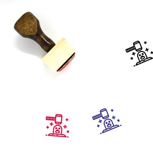 May include: A wooden rubber stamp with a red ink pad. The stamp features a line drawing of a hammer smashing a penguin with stars around it.