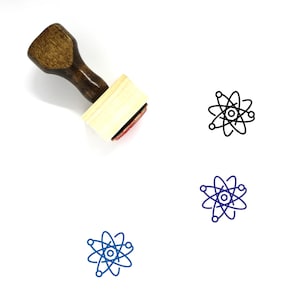 Puede incluir: Un sello de goma de madera con un mango marr&oacute;n y una base rectangular. El sello presenta un contorno negro de un &aacute;tomo con un n&uacute;cleo y electrones en &oacute;rbita.