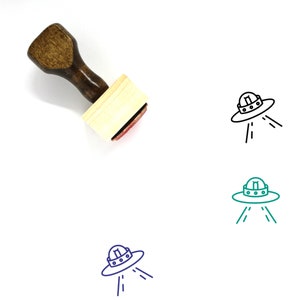 May include: Wooden rubber stamp with a black line drawing of a flying saucer with three beams of light coming from the bottom. The stamp is on a white background.