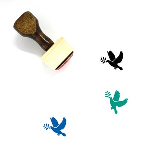 May include: A wooden stamp with a handle and a rectangular base. The stamp features a black silhouette of a dove carrying an olive branch in its beak. The stamp is shown next to three different coloured versions of the dove design: black, green, and blue.