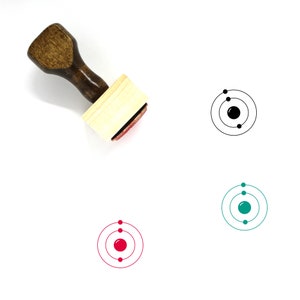 Puede incluir: Un sello de goma de madera con un mango negro y un bloque cuadrado de madera. El sello presenta una ilustración en blanco y negro de un átomo con un núcleo y dos electrones en órbita.