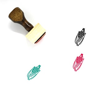 May include: A wooden stamp with a handle and a rectangular base. The stamp features a black and white line drawing of an ear of corn. The stamp is shown with three different colored impressions of the corn design.