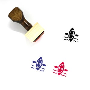May include: Wooden rubber stamp with a handle and a rectangular base. The stamp features a black silhouette of a canoe with paddles in the water. There are also three color variations of the canoe image in blue, red, and black.