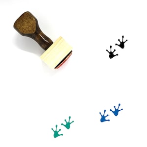 May include: A wooden stamp with a handle and a square base. The stamp is designed to create frog footprints. The image shows three sets of frog footprints in black, blue, and green.