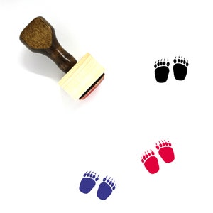 Peut inclure: Un tampon en caoutchouc en bois avec une poignée brune et une base rectangulaire. Le tampon présente un motif de deux empreintes de pattes d'ours en noir, rouge et bleu.