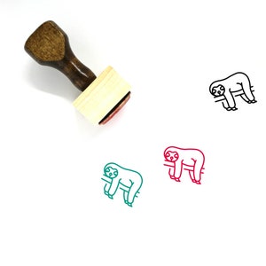 May include: A wooden rubber stamp with a red ink pad. The stamp features a line drawing of a sloth hanging from a branch. The sloth is outlined in black and has a green body and red legs.