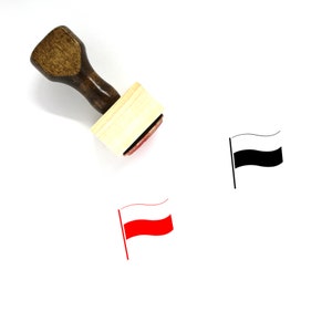 Puede incluir: Un sello de madera con una almohadilla de tinta roja. El sello presenta una bandera en blanco y negro con una franja roja. La bandera ondea al viento.