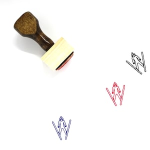 Puede incluir: Un sello de madera con una almohadilla de tinta roja. El sello presenta un dibujo lineal de una persona esquiando.