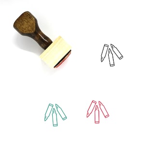 Puede incluir: Un sello de goma de madera con mango y base rectangular. El sello presenta un diseño de tres casquillos de bala en forma de triángulo. El diseño está delineado en negro, verde y rojo.