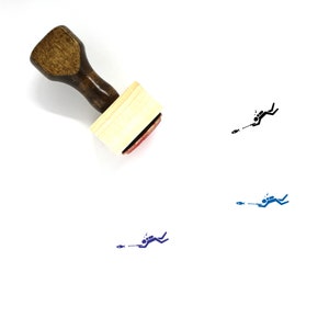 Puede incluir: Un sello de goma de madera con un mango marrón y una base rectangular de madera. El sello presenta una ilustración en blanco y negro de un buceador con un fusil de pesca submarina y un pez.