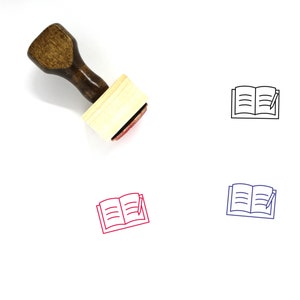 Puede incluir: Un sello de goma de madera con mango y base rectangular. El sello presenta un contorno negro de un libro abierto con un bolígrafo en la parte superior. El sello se muestra sobre un fondo blanco.