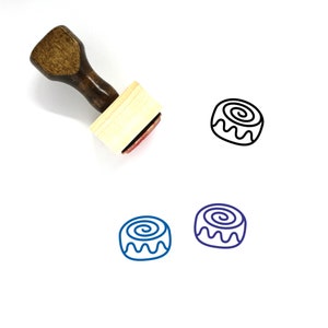 May include: A wooden rubber stamp with a cinnamon roll design. The stamp is brown with a red ink pad. The design is outlined in black and filled in with blue.