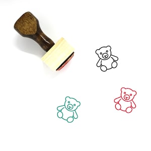 May include: Wooden stamp with a teddy bear design. The stamp is brown with a light wood base. The teddy bear is outlined in black, red, and green.