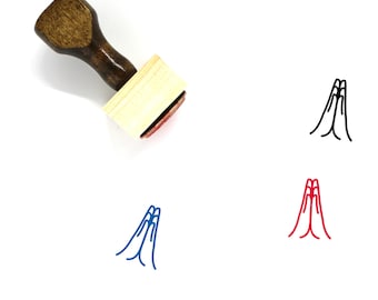 May include: A wooden stamp with a brown handle and a rectangular stamp head. The stamp head has a red ink pad and is next to three hand-drawn illustrations of hands in a prayer position, in black, blue, and red.