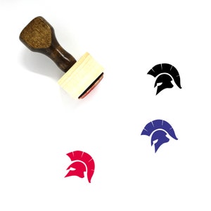 May include: A wooden rubber stamp with a brown handle and a rectangular wooden base. The stamp features a black silhouette of a Spartan helmet with a red, blue, and black outline.