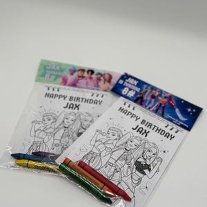 Op de afbeelding: Twee doorzichtige plastic zakken met kleurplaten en kleurpotloden. De kleurplaten bevatten een zwart-wit illustratie van een groep zangers met de tekst "HAPPY BIRTHDAY JAX". De zakken hebben ook de tekst "JAX is turning 8#".
