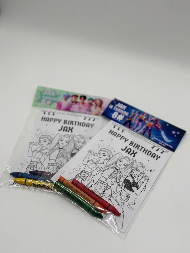 Op de afbeelding: Twee doorzichtige plastic zakken met kleurplaten en kleurpotloden. De kleurplaten bevatten een zwart-wit illustratie van een groep zangers met de tekst "HAPPY BIRTHDAY JAX". De zakken hebben ook de tekst "JAX is turning 8#".