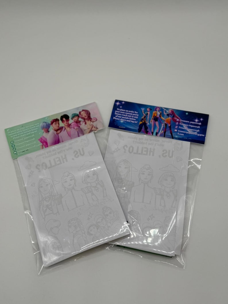 Op de afbeelding: Twee doorzichtige plastic verpakkingen met witte kleurplaten met contouren van stripfiguren. Elke verpakking heeft een kleurrijke header met tekst en afbeeldingen van mensen. De verpakkingen liggen op een wit oppervlak.
