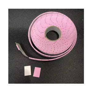 Puede incluir: Un rollo de cinta de espuma rosa con respaldo de papel, desenrollado sobre una superficie oscura. Dos peque&ntilde;os trozos rectangulares de la cinta est&aacute;n separados del rollo. La cinta est&aacute; dise&ntilde;ada con perforaciones espaciadas.