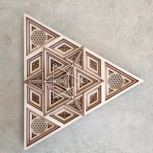 Peut inclure: Une œuvre d'art géométrique en bois en forme de triangle avec des motifs superposés complexes. La pièce présente une forme d'étoile centrale avec un motif de fleur de vie dans chaque coin.