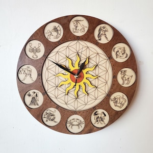 May include: A wooden clock with a brown background and a yellow sun in the center. The clock face is surrounded by twelve zodiac signs, each with a unique design. The clock hands are black.