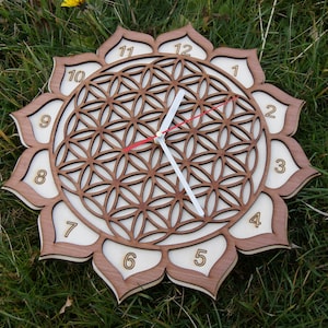 May include: A wooden clock with a flower-shaped frame and a white background. The clock face features a geometric pattern and the numbers 1 through 12 are displayed around the edge. The clock hands are white and red.