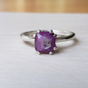 May include: A silver ring with a pink gemstone set in a square shape with a prong setting.