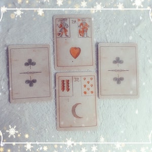 Op de afbeelding: Vijf tarotkaarten die in een kruisvorm op een wit, pluche oppervlak zijn gelegd. De kaarten zijn allemaal in vintage stijl met een cr&egrave;mekleurige achtergrond en bruine randen. De bovenste kaart toont twee figuren, een houdt een hart vast en de ander een schild. De kaart eronder toont een enkel rood hart. De kaart links toont twee groene klaver symbolen. De kaart rechts toont twee groene klaver symbolen. De onderste kaart toont een halve maan en negen rode harten.