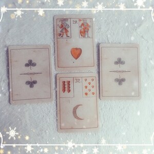 Puede incluir: Cinco cartas de tarot dispuestas en forma de cruz sobre una superficie blanca y peluda. Las cartas son todas de estilo vintage con un fondo crema y bordes marrones. La carta superior muestra dos figuras, una sosteniendo un coraz&oacute;n y la otra un escudo. La carta debajo muestra un solo coraz&oacute;n rojo. La carta de la izquierda muestra dos s&iacute;mbolos de tr&eacute;bol verde. La carta de la derecha muestra dos s&iacute;mbolos de tr&eacute;bol verde. La carta inferior muestra una luna creciente y nueve corazones rojos.