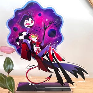 May include: A colorful acrylic stand featuring two cartoon characters against a purple and pink galaxy background. One character is black and white, the other is red and white. The stand has a black base.