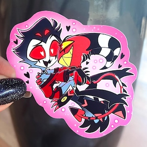 Puede incluir: Una pegatina rosa con dos personajes de dibujos animados abrazándose. Uno es rojo y amarillo, el otro azul y negro. La pegatina tiene un borde rosa con pequeños corazones negros y puntos blancos.