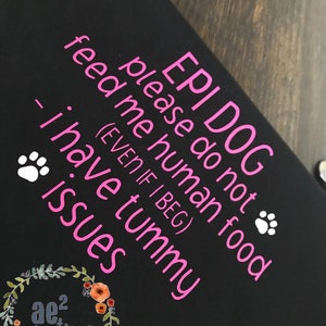 以下が含まれることがあります： ピンク色の文字で「EPI DOG please do not feed me human food (EVEN IF I BEG) - I have tummy issues」と書かれた黒い犬用バンダナ。足跡と花のロゴが含まれています。