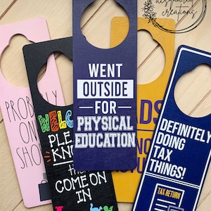 May include: A collection of door hangers in various colors, including pink, black, yellow, and navy blue. Each hanger has a unique message, such as "Went Outside for Physical Education" and "Definitely Doing Tax Things!"