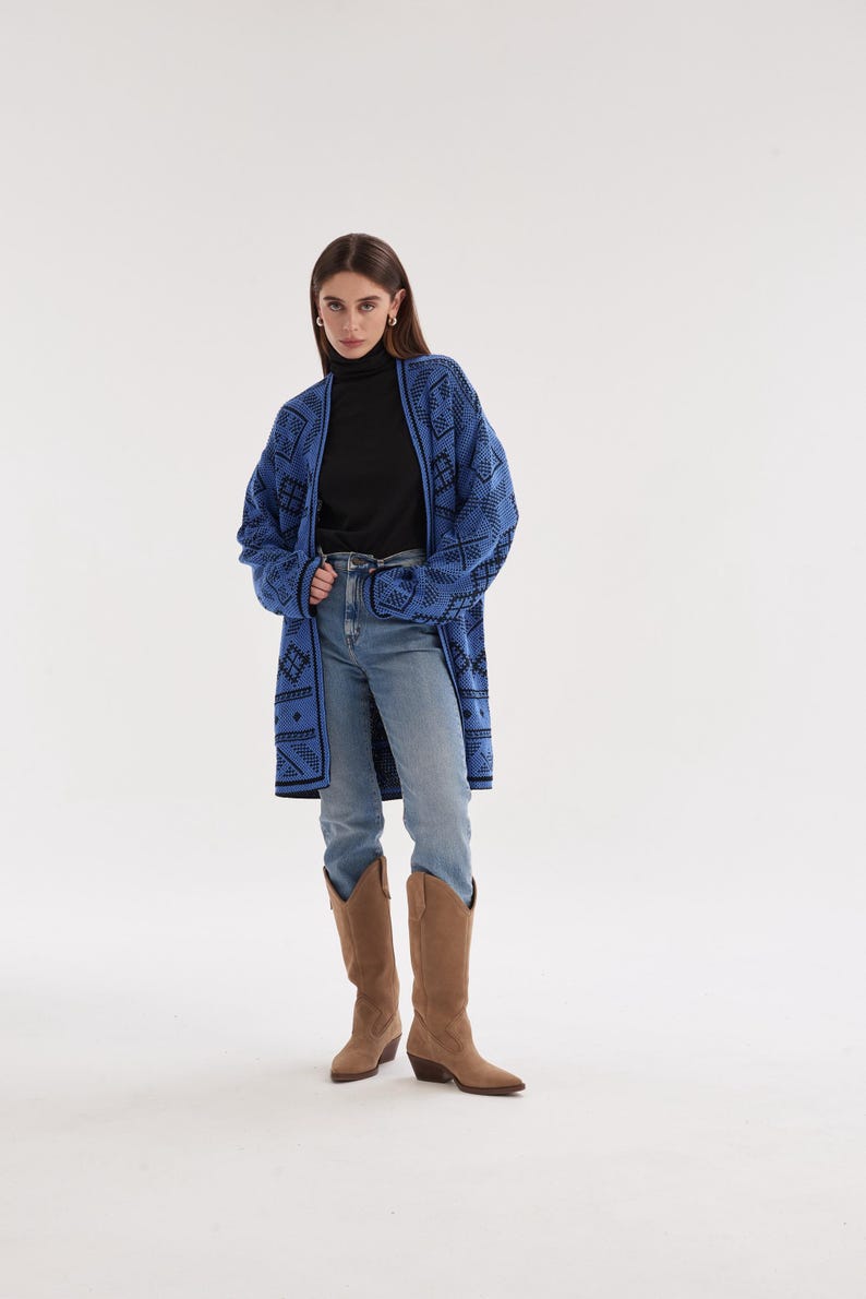 May include: A long-sleeved blue cardigan featuring a black geometric pattern, worn over a black turtleneck shirt, light blue denim jeans, and tan suede knee-high boots. The cardigan has an open front design with a black trim along the edges.