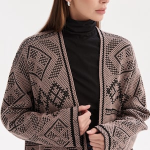 May include: A long-sleeved open-front cardigan featuring a tan and black geometric knit pattern. The garment has a solid black trim along the front opening and cuffs, with a textured knit construction throughout the body and sleeves.