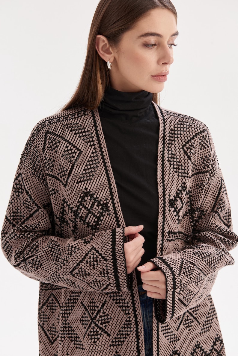 May include: A long-sleeved open-front cardigan featuring a tan and black geometric knit pattern. The garment has a solid black trim along the front opening and cuffs, with a textured knit construction throughout the body and sleeves.