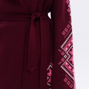 May include: A burgundy wrap cardigan with a matching tie belt. The sleeve features a geometric pattern in shades of pink and white. The cardigan is made of a soft knit material.