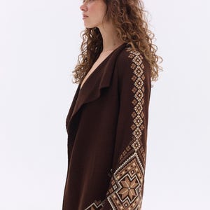 May include: A dark brown cardigan with a shawl collar and geometric patterned sleeves. The sleeves feature a repeating design in shades of brown, beige, and white. The cardigan is a medium weight and appears to be made of a soft knit material.