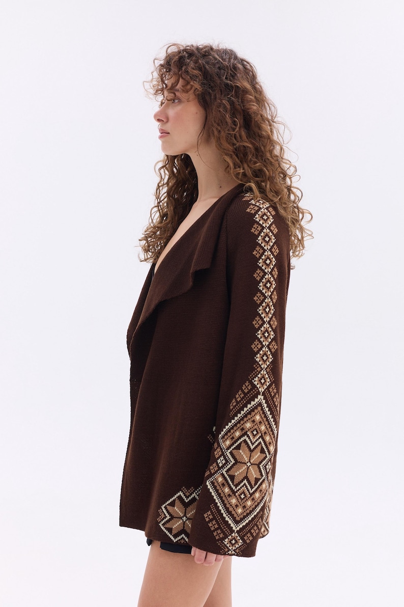 May include: A dark brown cardigan with a shawl collar and geometric patterned sleeves. The sleeves feature a repeating design in shades of brown, beige, and white. The cardigan is a medium weight and appears to be made of a soft knit material.