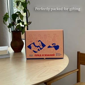 May include: A peach-colored gift box with a blue illustration of people relaxing indoors. The box has text in Ukrainian and English, and the words "Perfectly packed for gifting" are above the box.