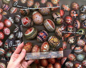 May include: A collection of intricately decorated Easter eggs, known as pysanky, with vibrant colours and intricate patterns. The eggs are displayed on a table, with some of them arranged in a circular pattern. The text "Авторські писанки Зої Сташук" is visible on the cards.
