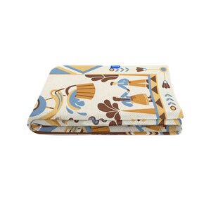 May include: Folded blanket with a cream background and a repeating pattern in shades of blue, brown, and gold. The design includes stylized figures, floral elements, and geometric shapes. The blanket is folded neatly, showcasing the detailed pattern.