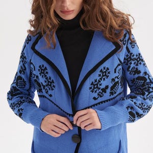 May include: A long blue cardigan with black trim and a black floral pattern. The cardigan has a single button closure and two pockets.