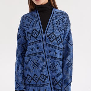 May include: A long-sleeved open-front cardigan in bright blue with a repeating black geometric pattern. The knit garment features a V-neckline, straight hem, and black trim along the edges, showcasing a detailed diamond and line motif throughout.