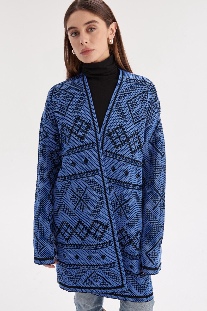 May include: A long-sleeved open-front cardigan in bright blue with a repeating black geometric pattern. The knit garment features a V-neckline, straight hem, and black trim along the edges, showcasing a detailed diamond and line motif throughout.