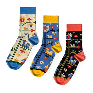 May include: Three pairs of colorful socks with a folk art design featuring a tree, flowers, birds, and a woman in a dress. The socks are in blue, yellow, and red.