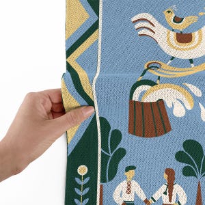 May include: A section of a blue fabric with a folk art design. The design includes a large white bird with a smaller bird on its back, a brown bucket, and figures in traditional clothing. The fabric has yellow, green, and white accents.
