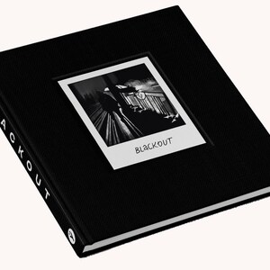 Pode incluir: Livro preto com uma foto em preto e branco de uma pessoa subindo uma escada. O t&iacute;tulo do livro &eacute; "BLACKOUT" em texto branco.