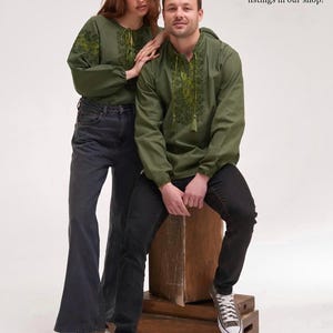 May include: Two people wearing olive green embroidered shirts and dark denim jeans. The shirts have a drawstring neckline and long sleeves. The text "Matching his & hers available" and "Pair up in style - explore both listings in our shop!" is visible.